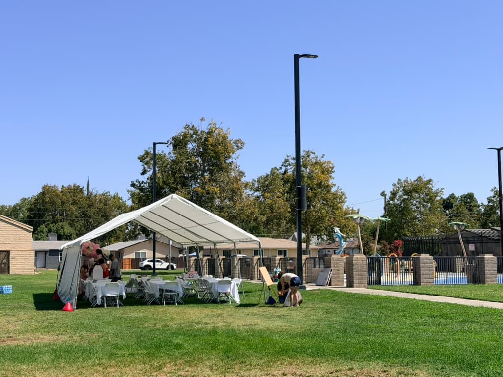 White canopy and guest seating set up on grass beside a swimming pool.