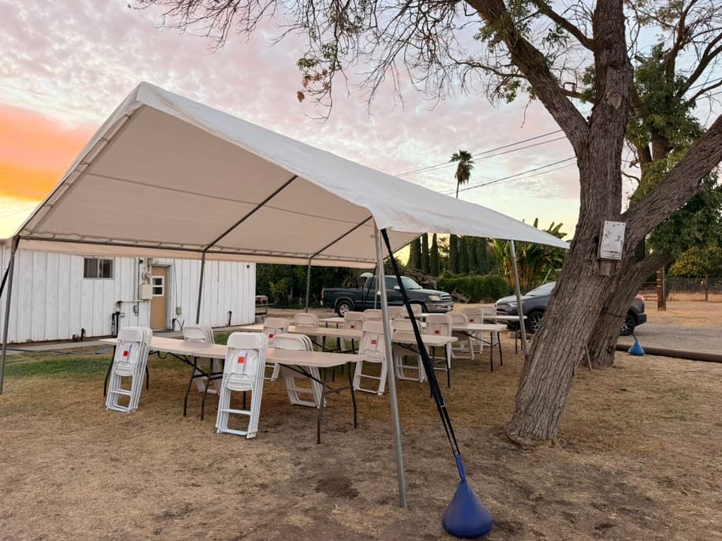 White canopy sheltering folding tables and stacked white chairs beneath a sunset sky.