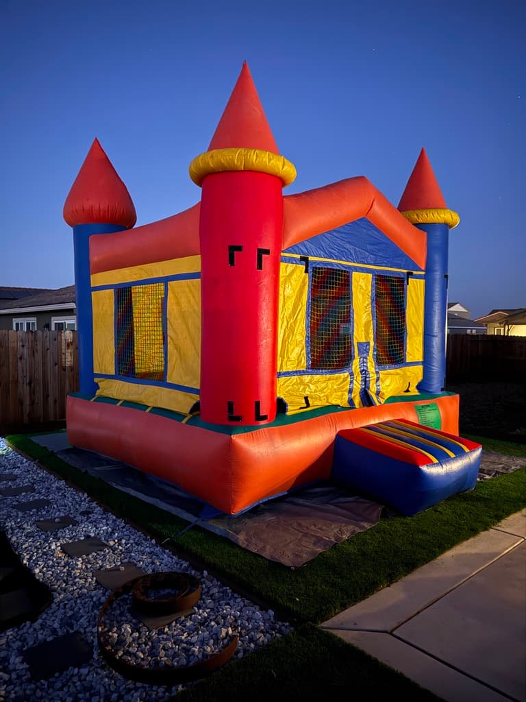 Red, yellow, and blue castle bounce house illuminated at dusk.
