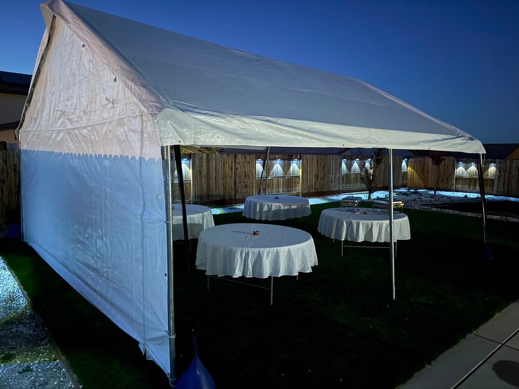 White canopy with round tables and white linens illuminated at night.