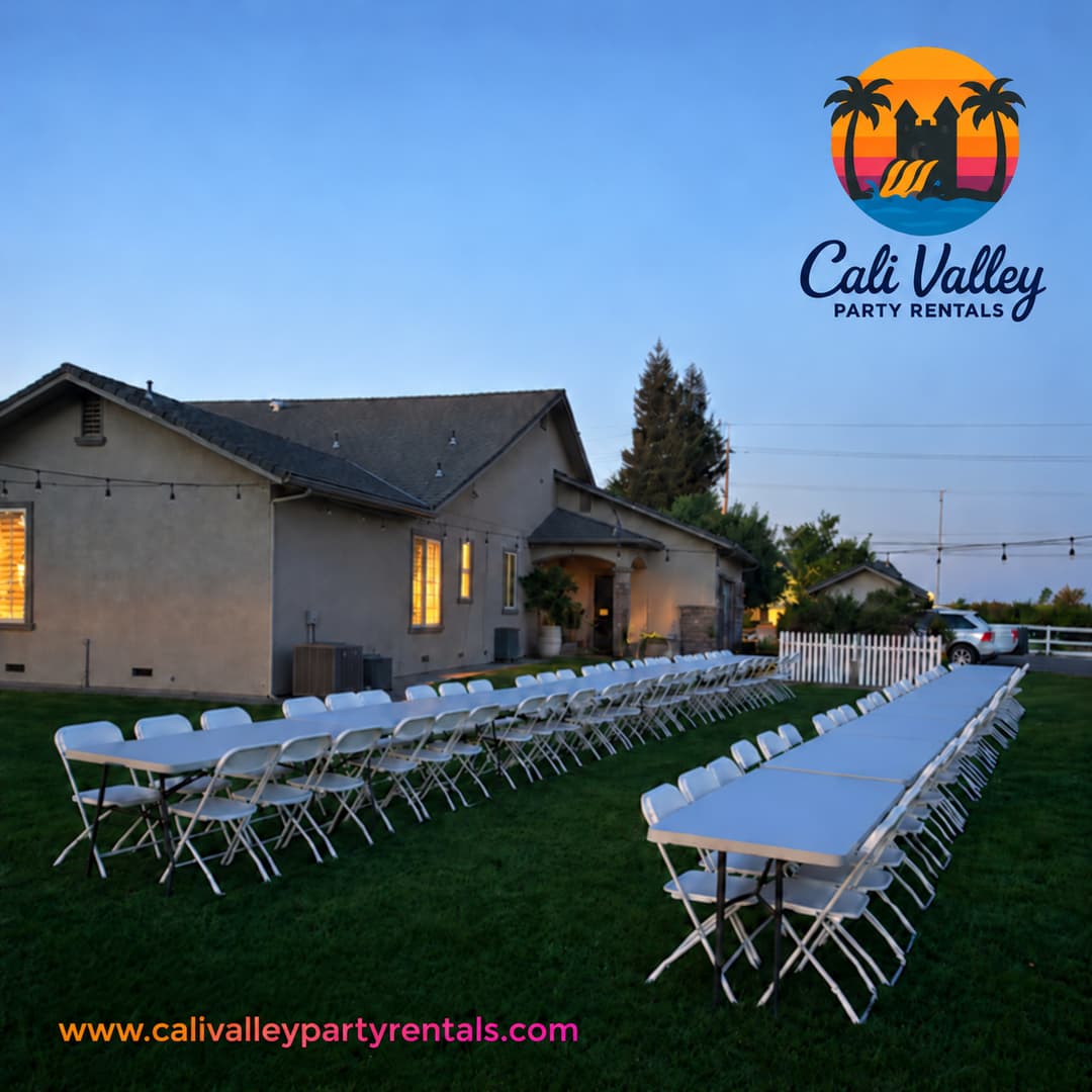 Long rows of white rectangular folding tables and white folding chairs on a lawn beside a gray home at dusk. Clear sky at upper left. The official CVPR logo and navy script business wordmark are at upper right. The lower-left footer contains only www.calivalleypartyrentals.com in sunset orange-to-pink lettering.